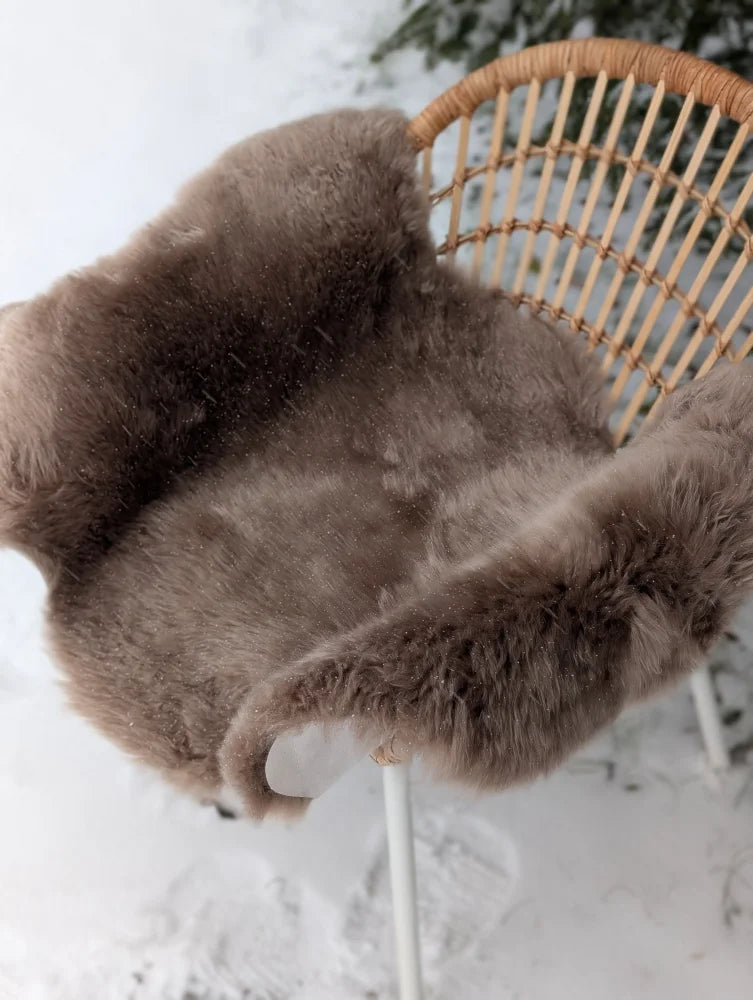 Brown sheepskin chair cover draped over wicker chair made from medium taupe merino sheepskin