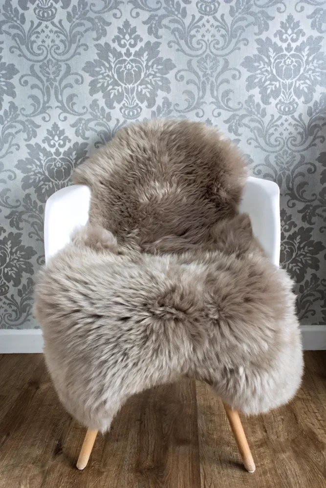 A plush medium taupe merino sheepskin throw draped over a white chair with wooden legs arriving mid october