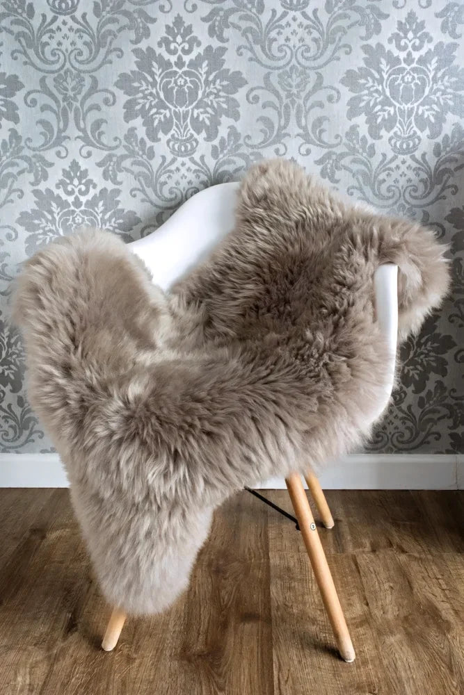 A plush medium taupe merino sheepskin chair cover draped over a white modern chair with wooden legs