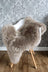 A plush medium taupe merino sheepskin chair cover draped over a white modern chair with wooden legs