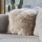 Fluffy beige faux fur sheepskin cushion with cotton back resting on textured gray couch for cozy decor
