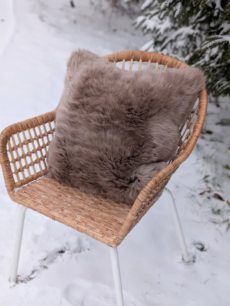 A cozy medium taupe merino sheepskin cushion with a soft cotton back on a woven wicker chair with white metal legs