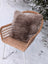 A cozy medium taupe merino sheepskin cushion with a soft cotton back on a woven wicker chair with white metal legs