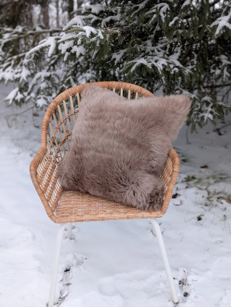 A soft taupe merino sheepskin cushion with cotton backs resting on a woven wicker chair