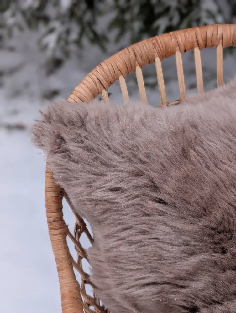 A soft gray merino sheepskin cushion with a cotton backs cover resting on a woven wicker chair
