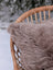 A soft gray merino sheepskin cushion with a cotton backs cover resting on a woven wicker chair