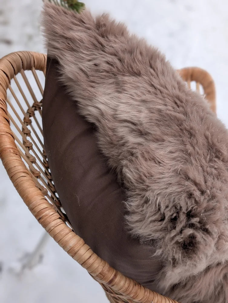 A plush taupe merino sheepskin cushion cover with cotton backs draped over a dark brown cushion in a wicker chair