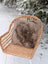 A cozy fluffy medium taupe merino sheepskin cushion with cotton backs resting on a woven wicker chair