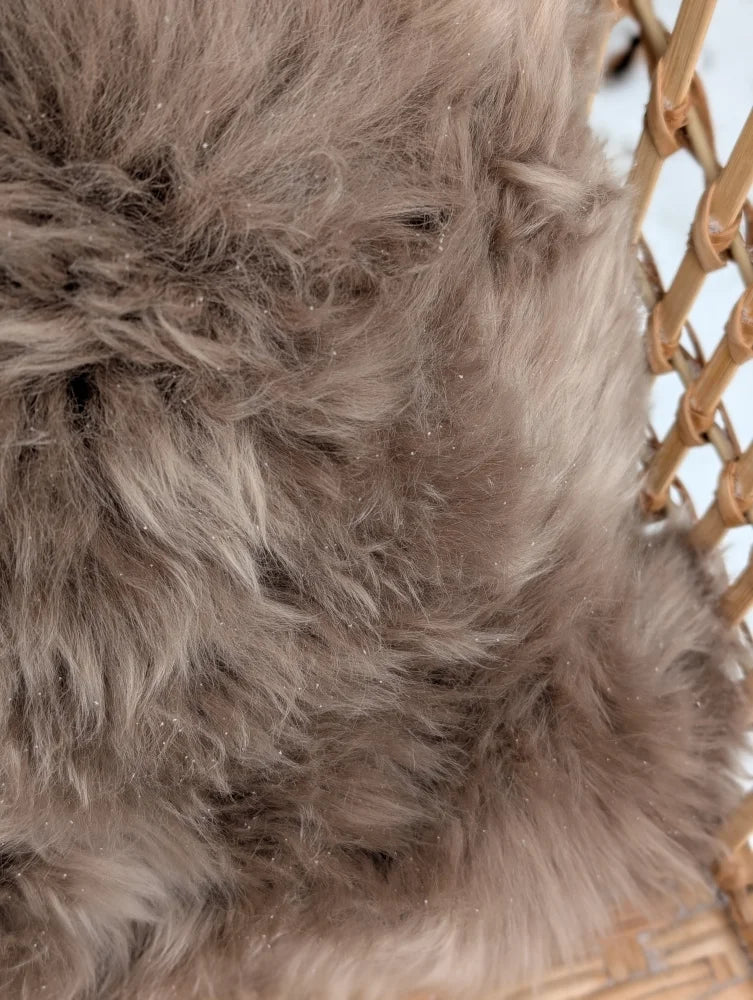A medium taupe merino sheepskin cushion cover with a plush gray faux fur texture and soft cotton backs