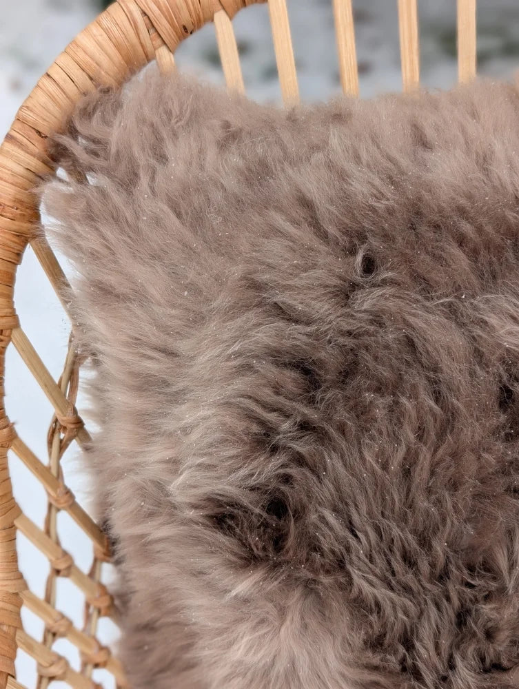 Medium taupe merino sheepskin cushion with soft gray sheepskin cushion cover on woven wicker chair with cotton backs