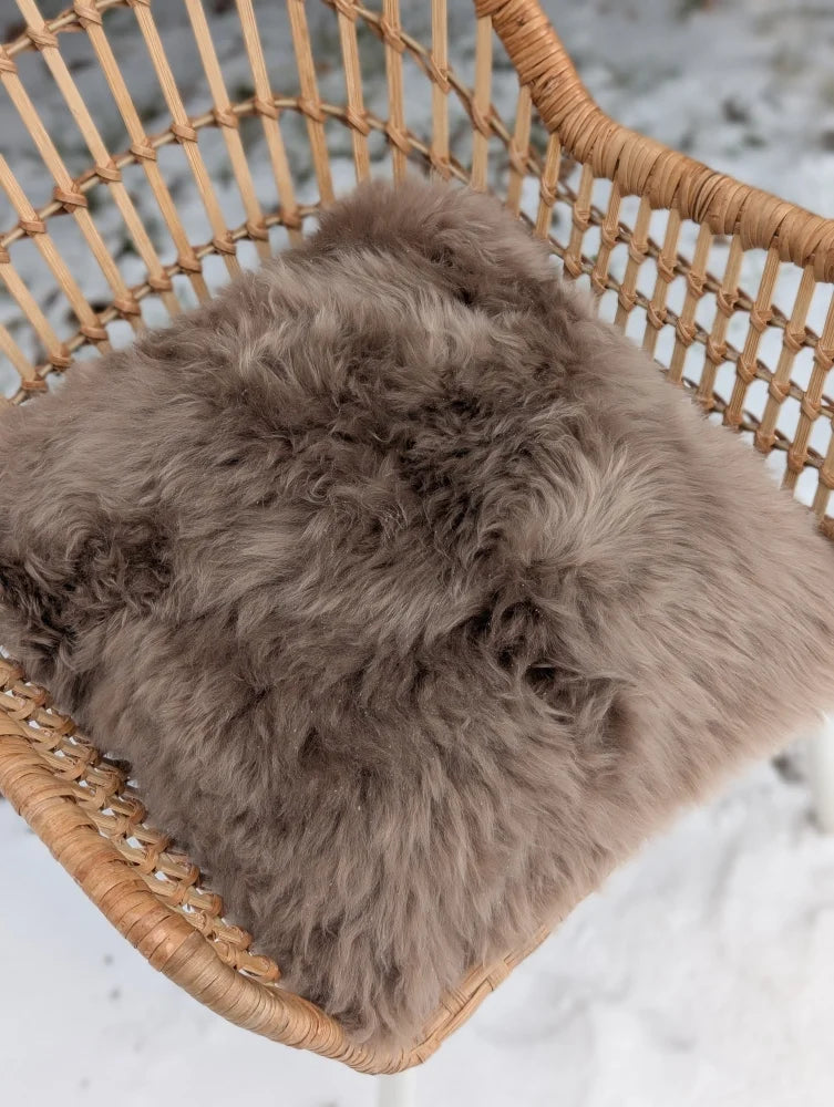 A medium taupe merino sheepskin cushion with soft cotton backs resting on a woven wicker chair