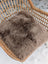 A medium taupe merino sheepskin cushion with soft cotton backs resting on a woven wicker chair