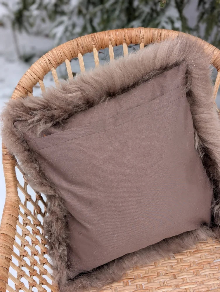 A cozy medium taupe merino sheepskin cushion with plush faux fur trim and cotton backs on a wicker chair