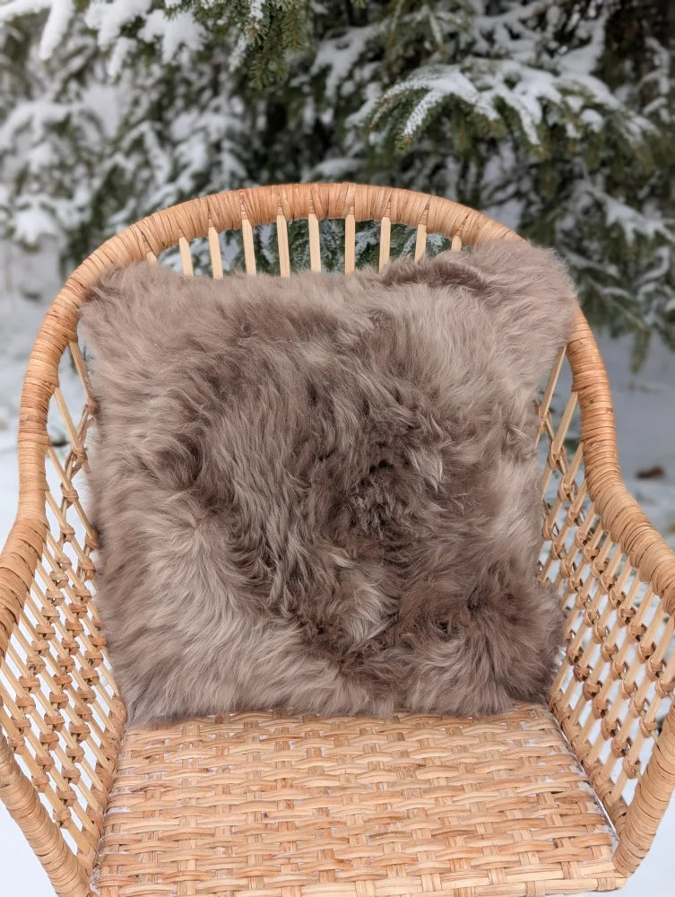 A medium taupe merino sheepskin cushion with cotton back resting on a woven wicker chair as a sheepskin cushion cover