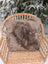 A medium taupe merino sheepskin cushion with cotton back resting on a woven wicker chair as a sheepskin cushion cover