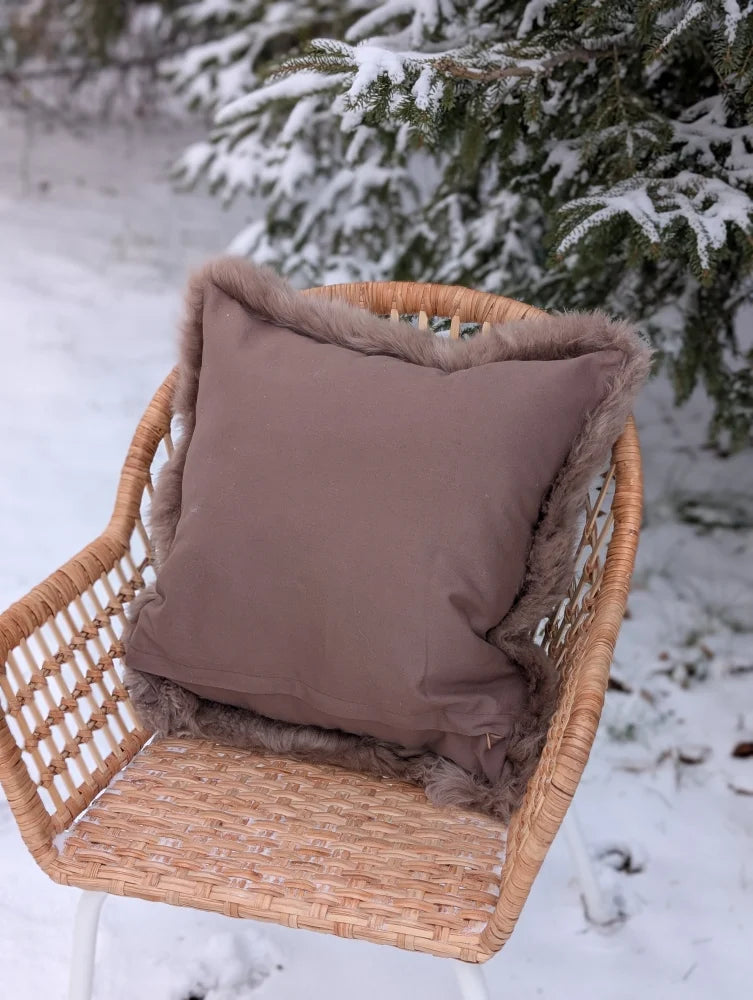 A cozy medium taupe merino sheepskin cushion cover with soft fuzzy brown trim on a wicker chair with cotton backs