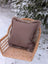 A cozy medium taupe merino sheepskin cushion cover with soft fuzzy brown trim on a wicker chair with cotton backs