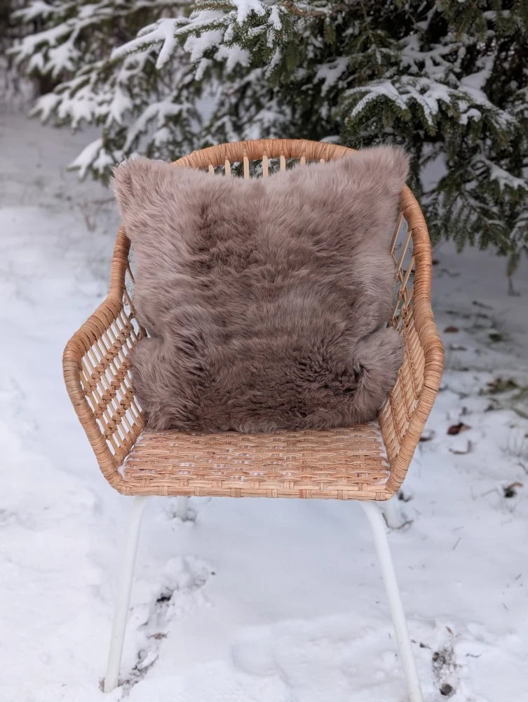 Medium taupe merino sheepskin cushion cover with soft faux fur front and cotton backs on wicker chair