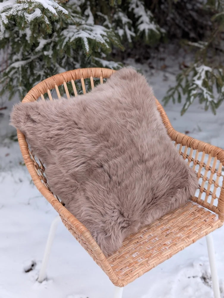 A plush taupe merino sheepskin cushion with soft fluffy texture on cotton backs rests on a woven wicker chair