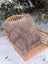 A plush taupe merino sheepskin cushion with soft fluffy texture on cotton backs rests on a woven wicker chair