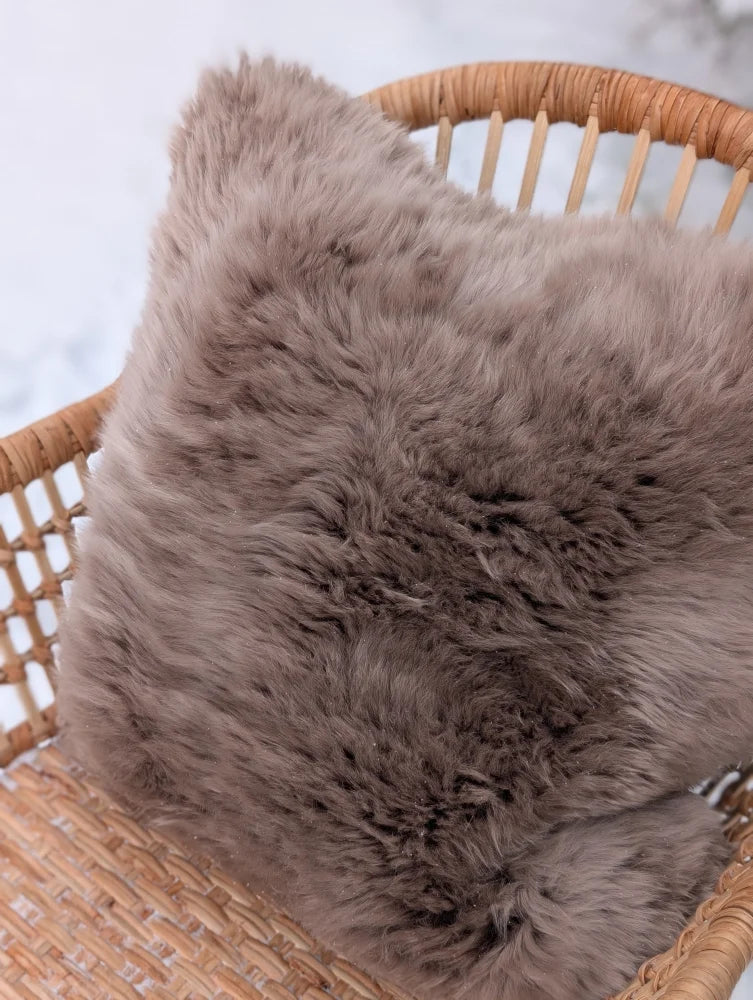 A medium taupe merino sheepskin cushion with soft fluffy texture and cotton backs on a woven wicker chair