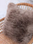 A medium taupe merino sheepskin cushion with soft fluffy texture and cotton backs on a woven wicker chair