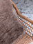 Medium taupe merino sheepskin cushion cover made of soft fluffy wool with cotton backs draped over wicker chair