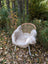 A cozy beige british isles sheepskin throw draped over a woven wicker chair with white metal legs