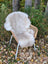 A cozy off-white british isles sheepskin rug draped over a wicker chair with white metal legs