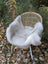 A plush off-white british isles sheepskin throw draped over a woven wicker chair with white metal legs