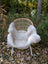 A cozy off-white british isles sheepskin throw draped over a woven wicker chair with white metal legs