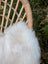 A soft off-white british isles sheepskin rug with plush texture resting on a wicker outdoor chair frame