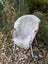 A cozy off-white british isles sheepskin rug draped over a woven wicker chair with white metal legs
