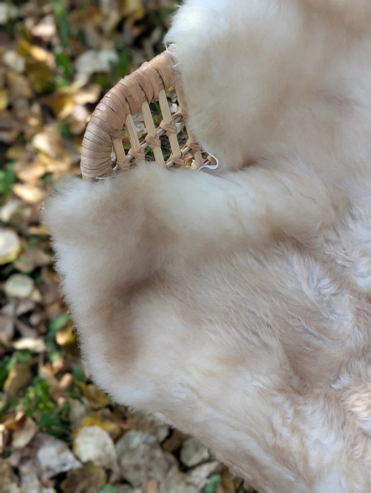 A cream-colored soft faux british isles sheepskin blanket draped over a woven wicker chair arm