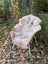 A soft light beige british isles sheepskin rug draped over a wicker chair with white metal legs