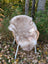 A soft light beige british isles sheepskin rug draped over a wicker chair with white metal legs