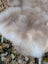 A soft cream-colored british isles sheepskin throw with plush fluffy faux fur draped over a woven chair back