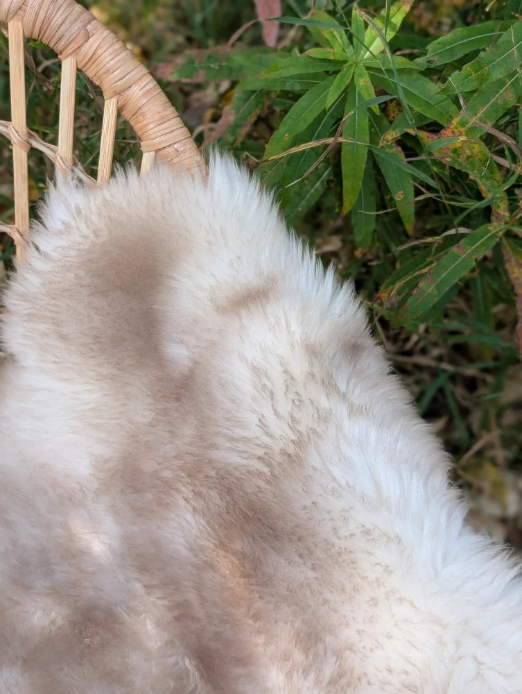 A soft fluffy white and beige british isles sheepskin faux fur throw draped over a woven wicker chair