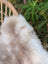 A soft fluffy white and beige british isles sheepskin faux fur throw draped over a woven wicker chair