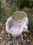 A soft light beige british isles sheepskin throw draped over a woven rattan chair with white metal legs