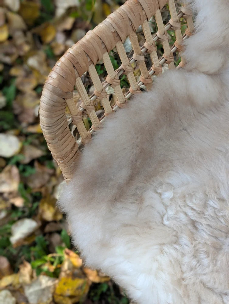 A soft cream-colored british isles sheepskin rug draped over the woven wicker edge of a basket