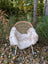 A soft fluffy white british isles sheepskin throw draped over a woven rattan chair with metal legs
