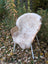 A soft off-white british isles sheepskin rug draped over a wicker chair with white metal legs