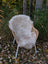 A soft cream-colored british isles sheepskin rug draped over a wicker chair with white metal legs