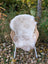 A soft cream-colored british isles sheepskin rug draped over a wicker chair with white metal legs