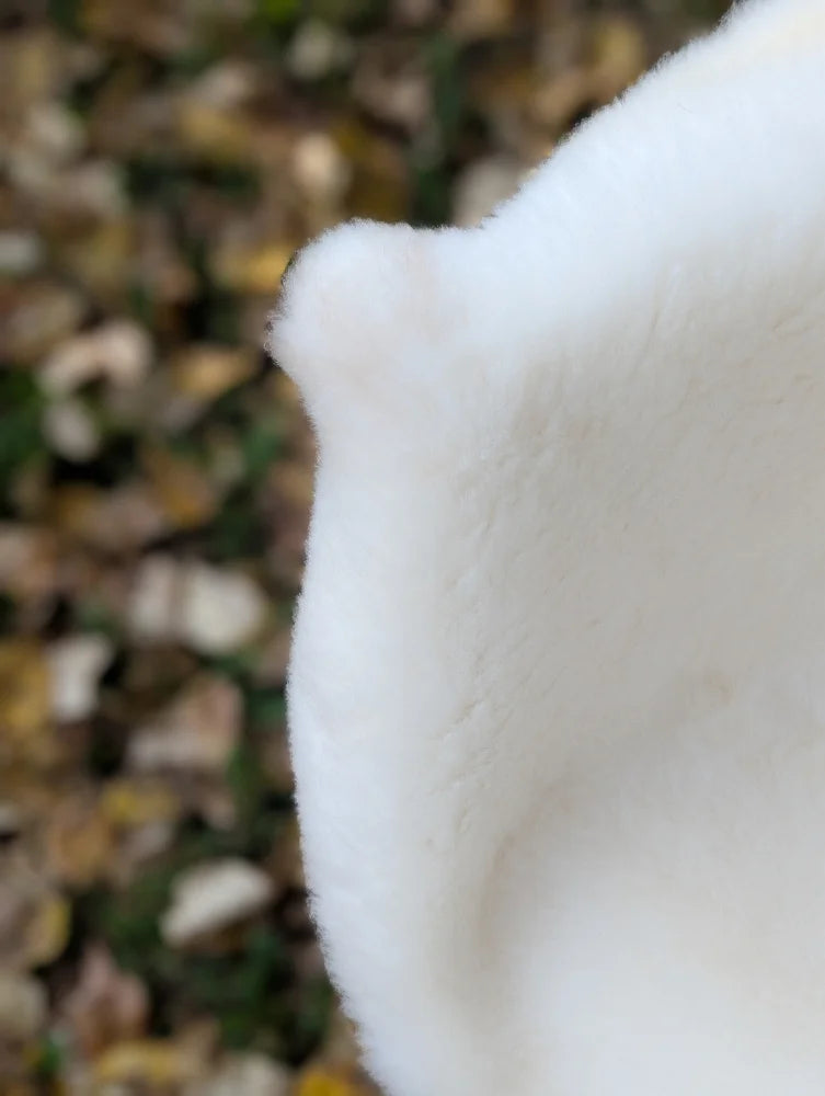 A soft white fluffy british isles sheepskin with a rounded edge and textured surface perfect for cozy decor