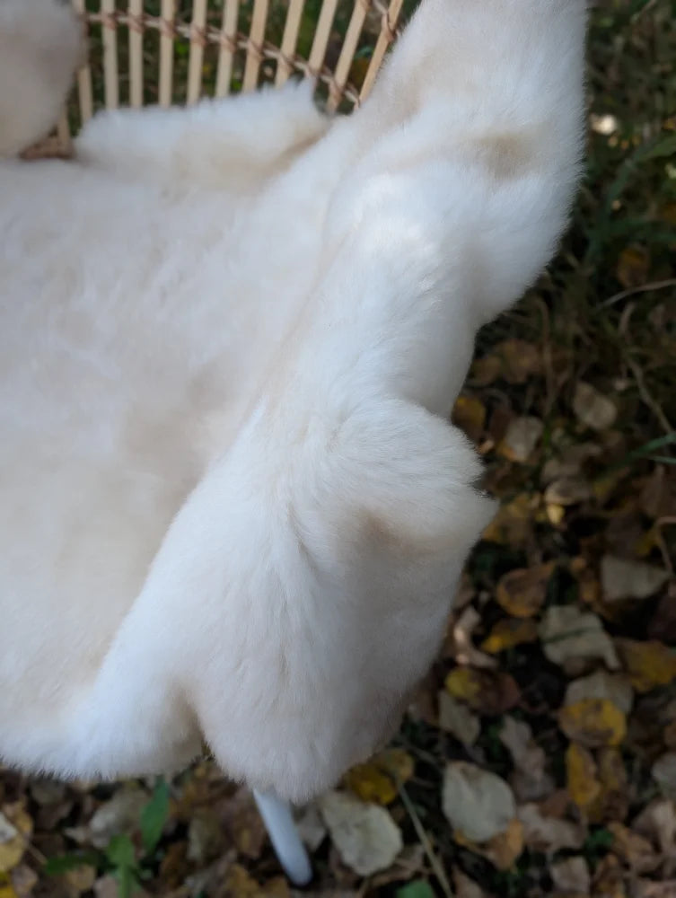 A plush creamy white british isles sheepskin faux fur blanket draped over a woven wicker chair