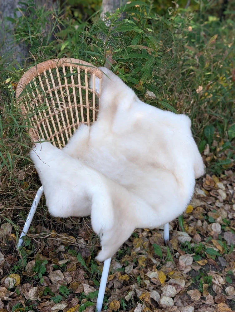 A soft creamy white british isles sheepskin faux fur throw draped over a wicker chair for cozy comfort
