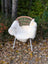 A cozy white british isles sheepskin blanket draped over a woven wicker chair with metal legs