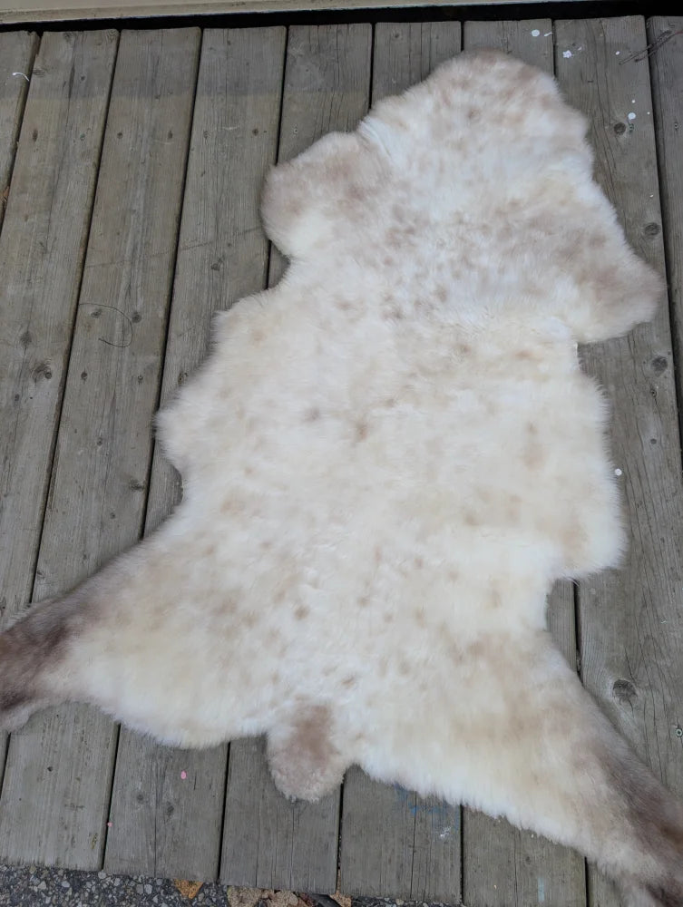 A soft natural white and light brown british isles sheepskin rug with fluffy texture on a wooden deck